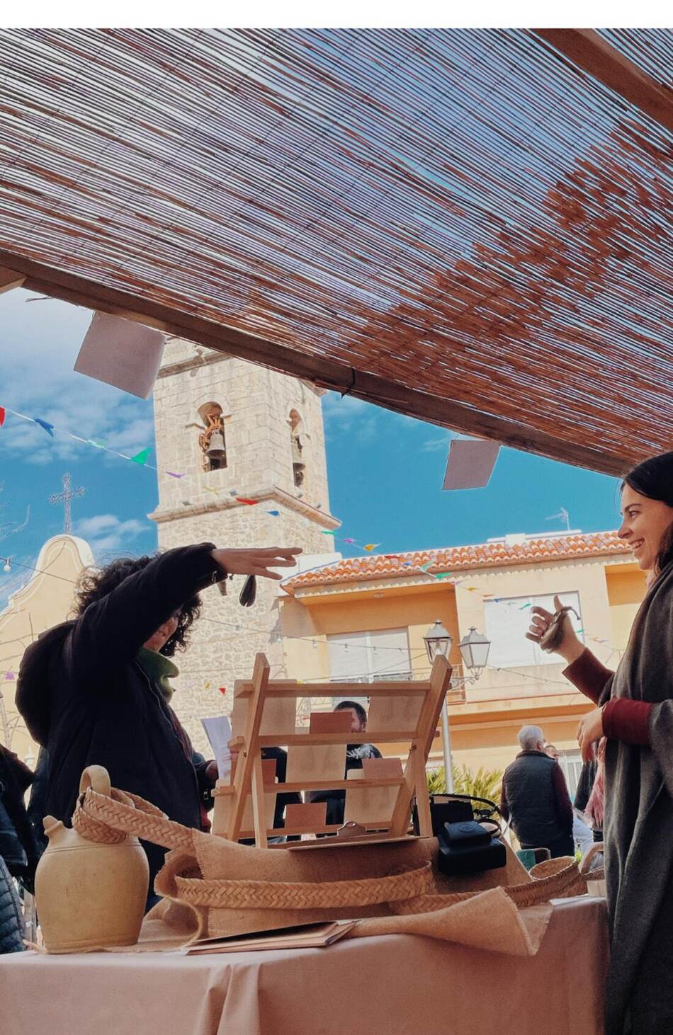 Parada de cistelleria i espart a la plaça d'un poble, amb el campanar al fons