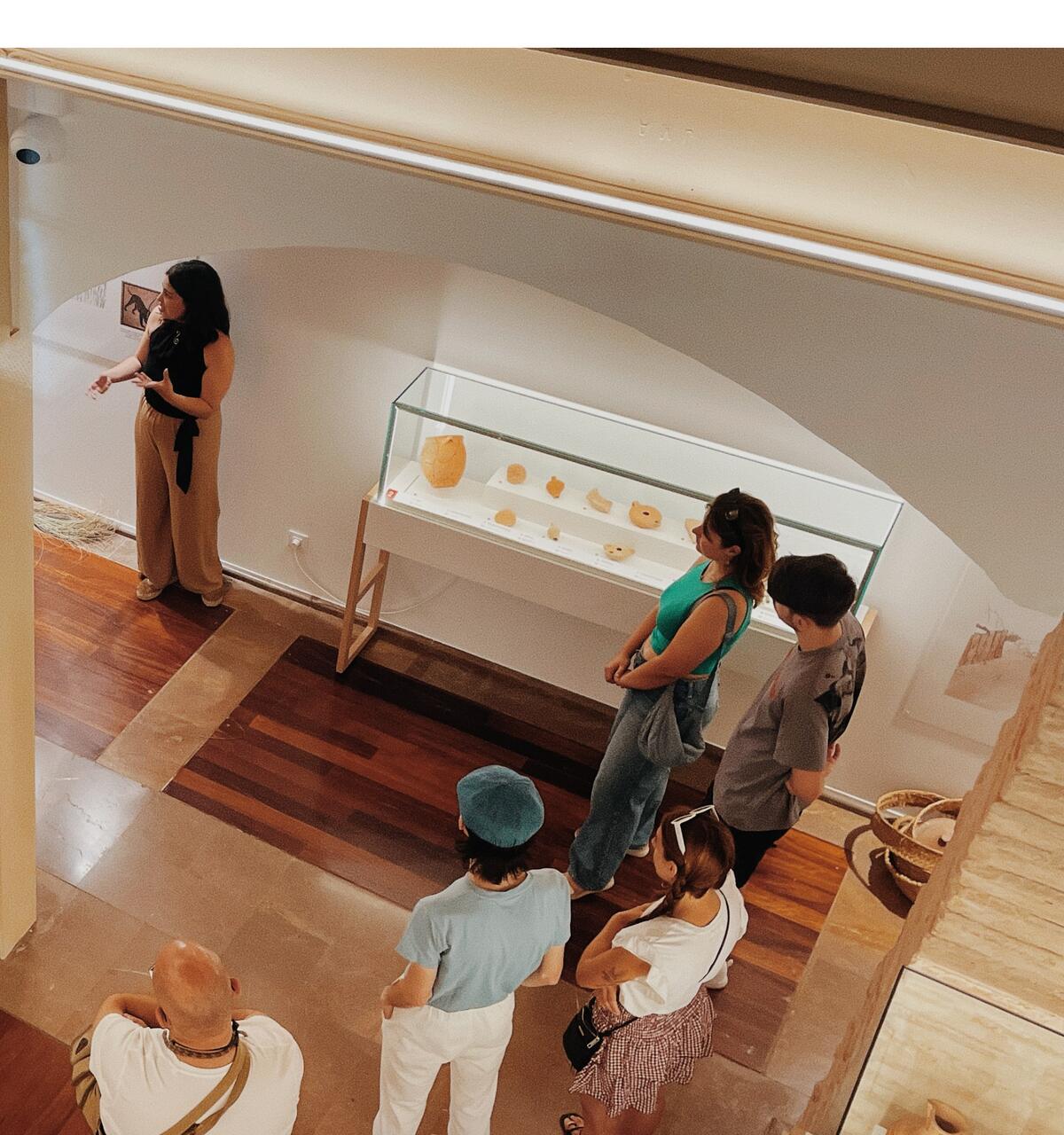 Visita guiada en una sala de museu, amb un grup davant d'una vitrina de ceràmica